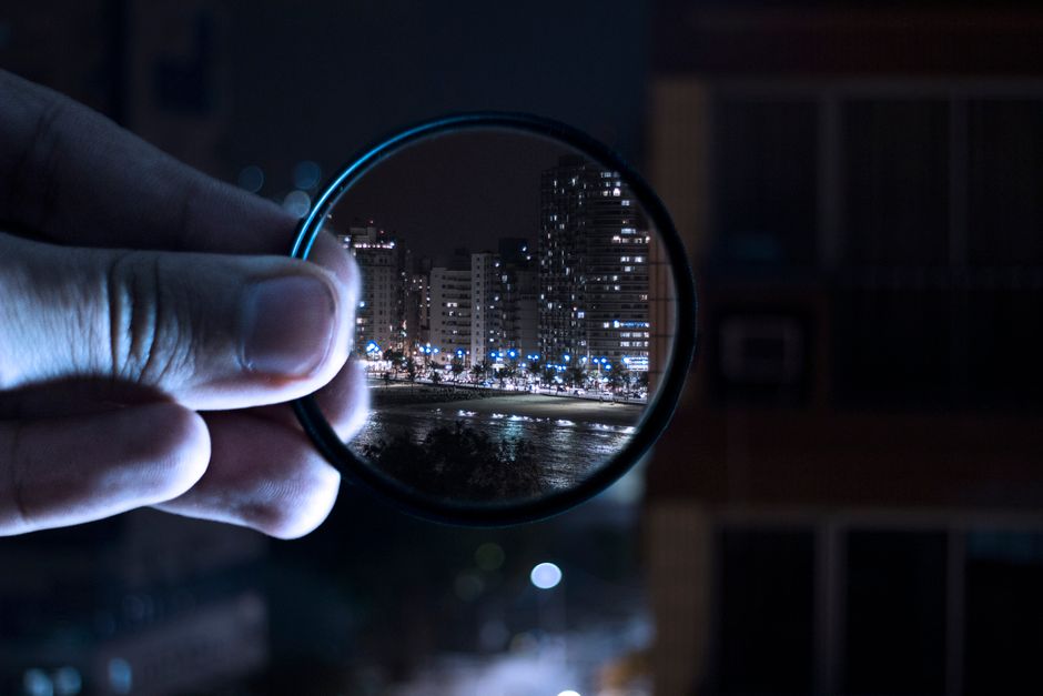 A hand holding a lens filter enhances a vibrant city nightlife scene.